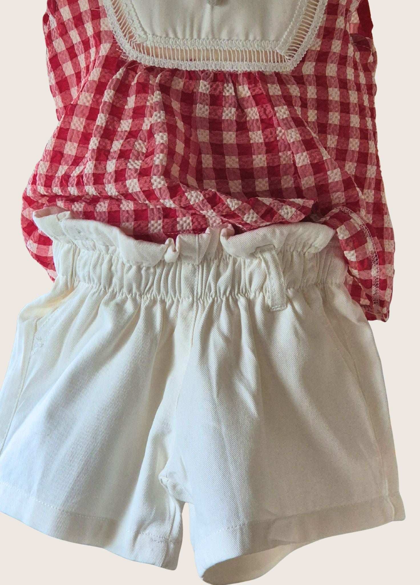 Red and white checkered top with white shorts on a beige background