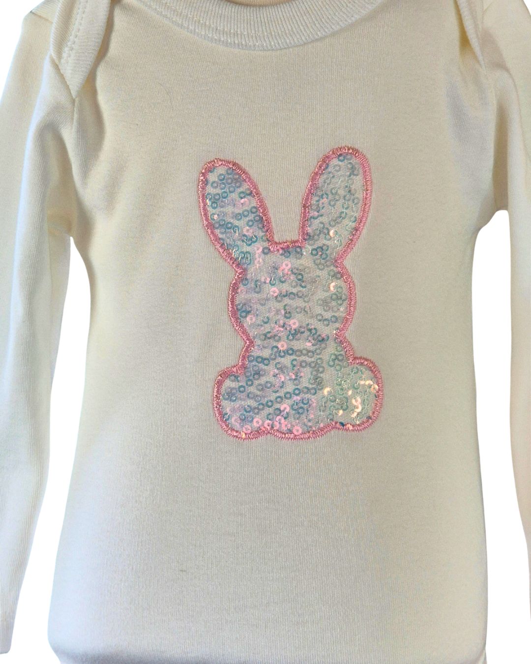 An off-white long-sleeve baby bodysuit featuring a sequined bunny applique on the chest with a pink border.