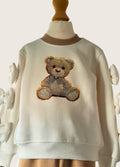 White sweater with a teddy bear design on a mannequin against a white background